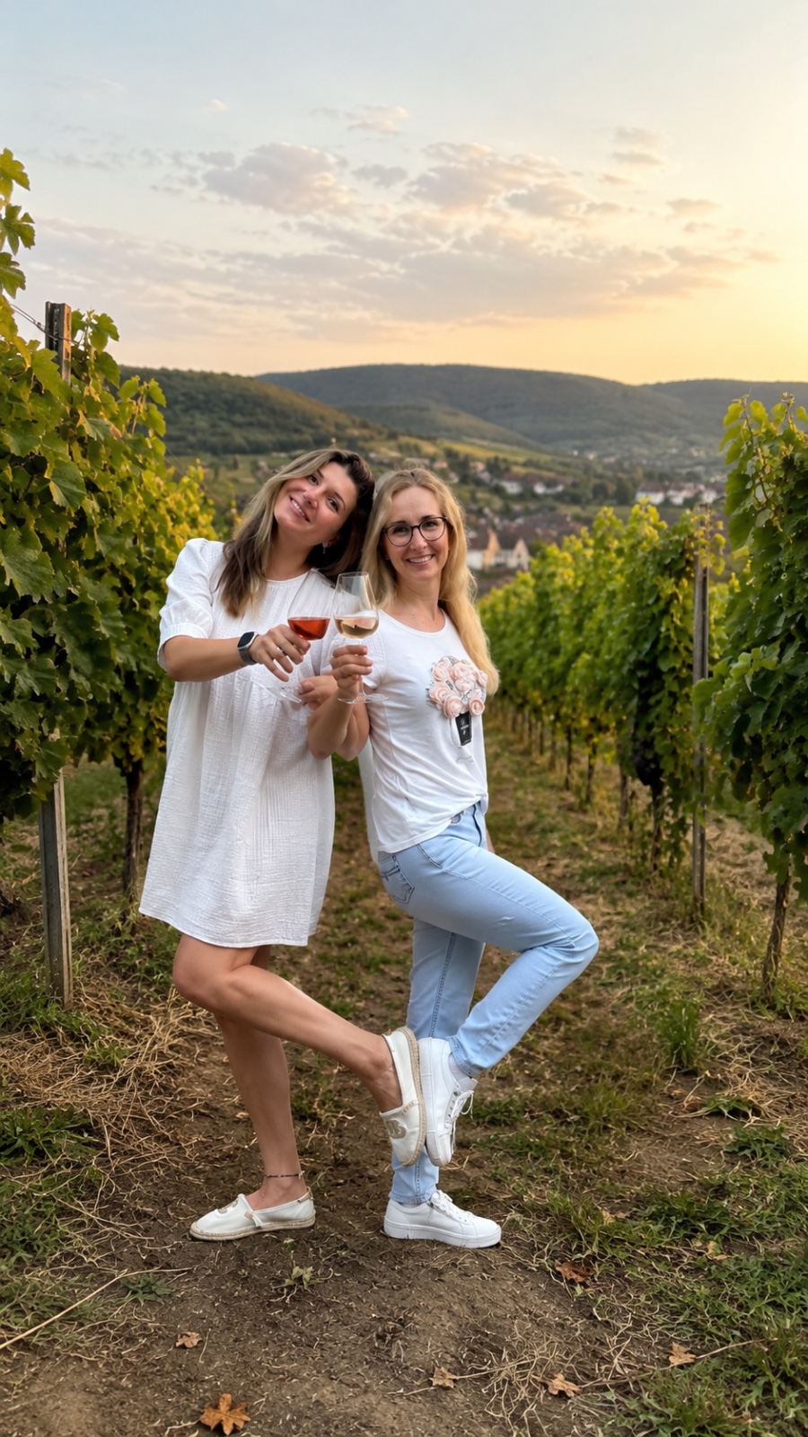 Oksana und Polina mit Weingläsern zwischen den Rebzeilen, im Hintergrund das Rheintal