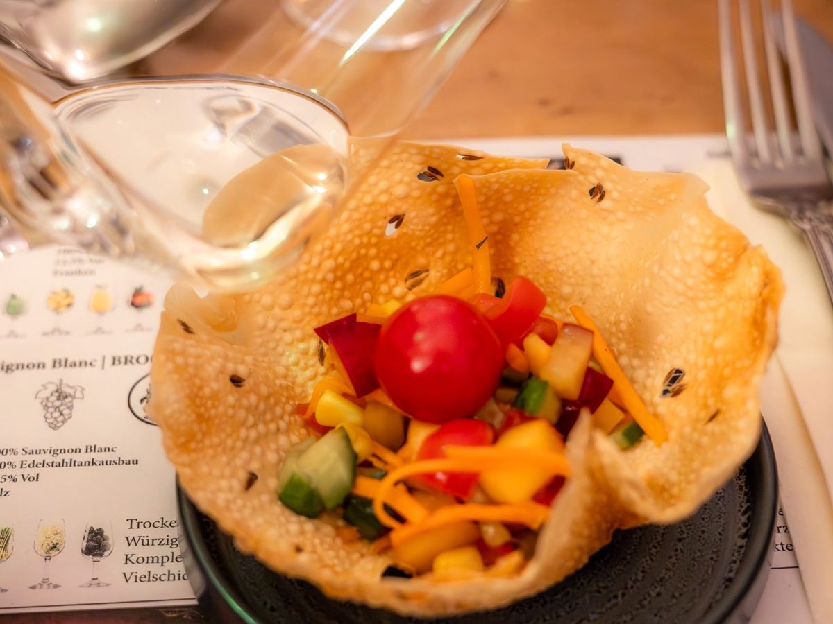 Knuspriges Papadam-Körbchen mit buntem Gemüsesalat neben Weingläsern und der Menükarte des Abends