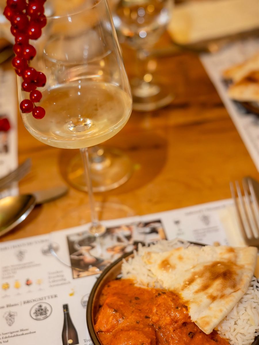 Weißweinglas mit roten Johannisbeeren garniert, daneben eine Schale Curry mit Naan