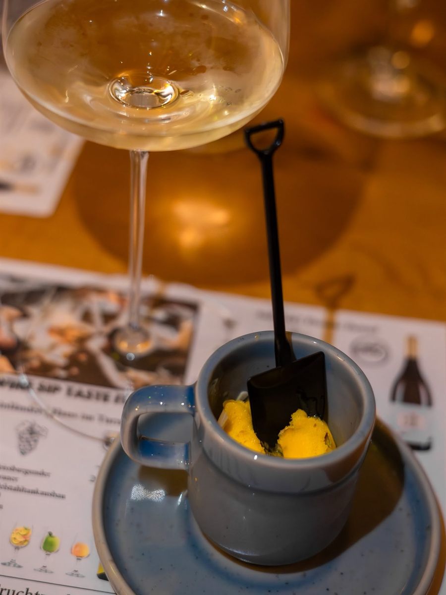 Weißweinglas über einer Tasse mit Mango-Dessert und kleiner Servierschaufel