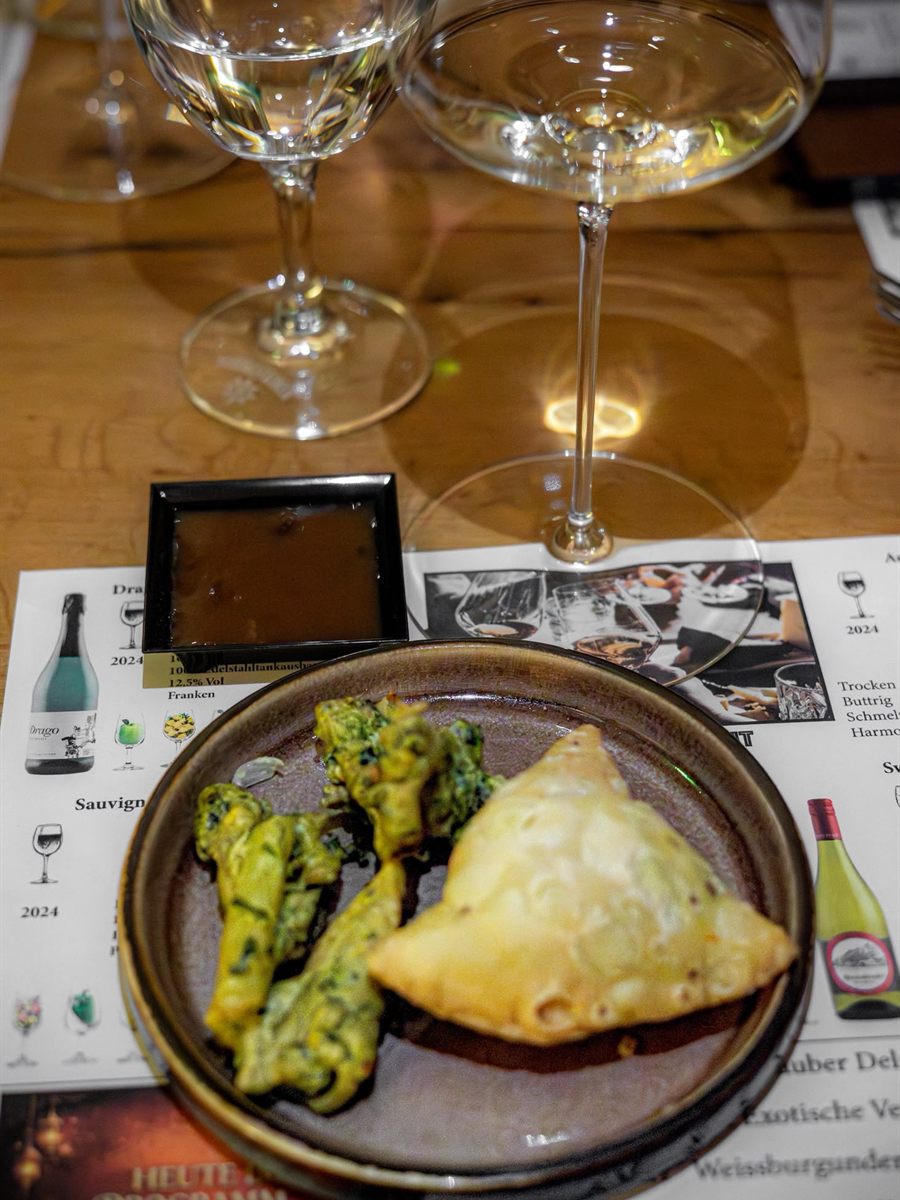 Teller mit Samosa und grünen Gemüsespießen neben zwei Weingläsern