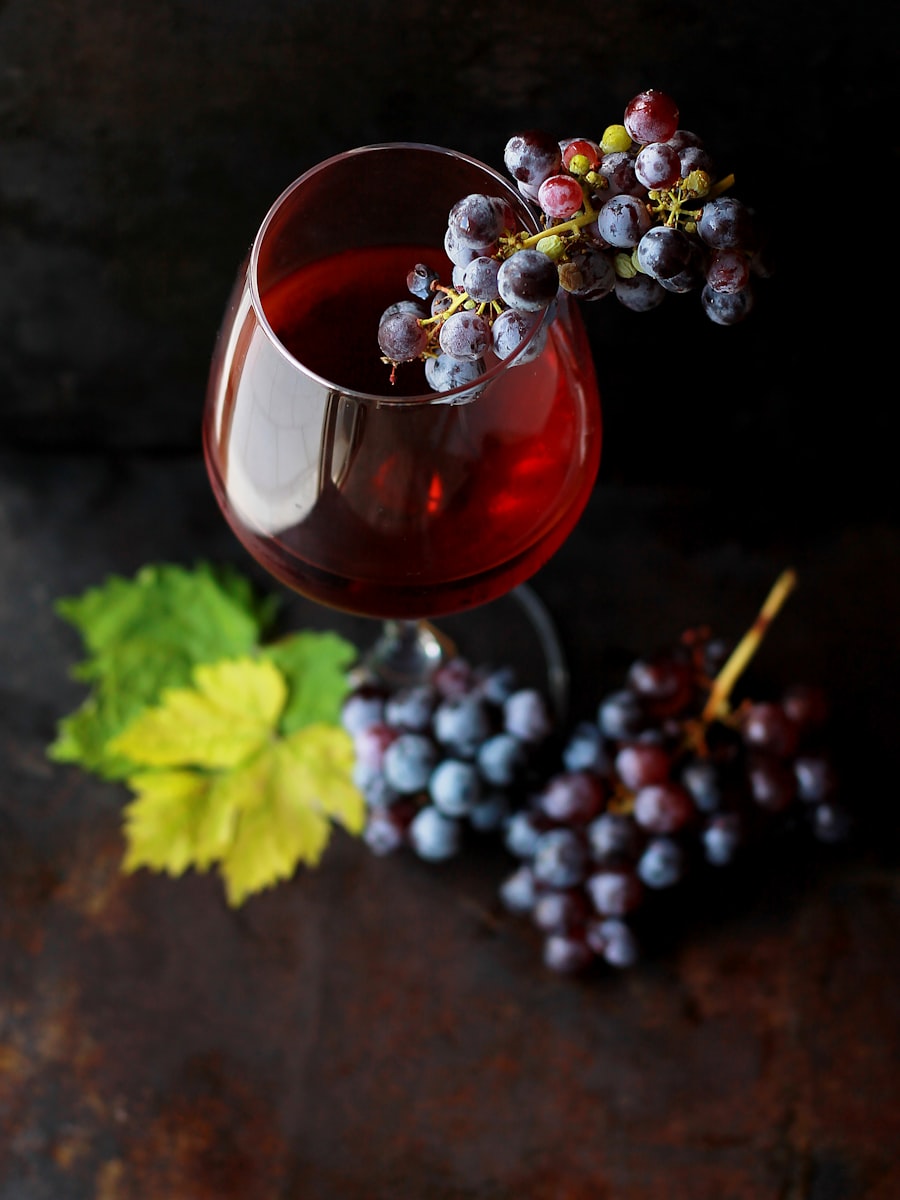 Glas Rotwein neben dunklen Weintrauben auf einem Holztisch